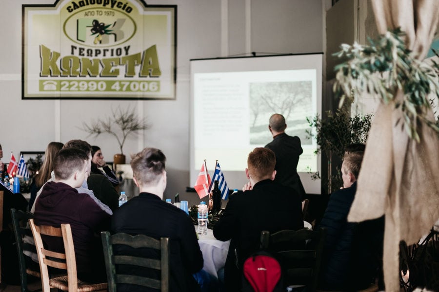 visitors listening to a guide at Konstas Olive Tours plant and watching a video